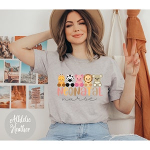 Puede incluir: Una camiseta gris con un gr&aacute;fico de cinco animales de dibujos animados y el texto "NEONATAL nurse". Los animales son una jirafa, una cebra, un cerdo, un le&oacute;n y un koala. La camiseta es de color gris jaspeado.