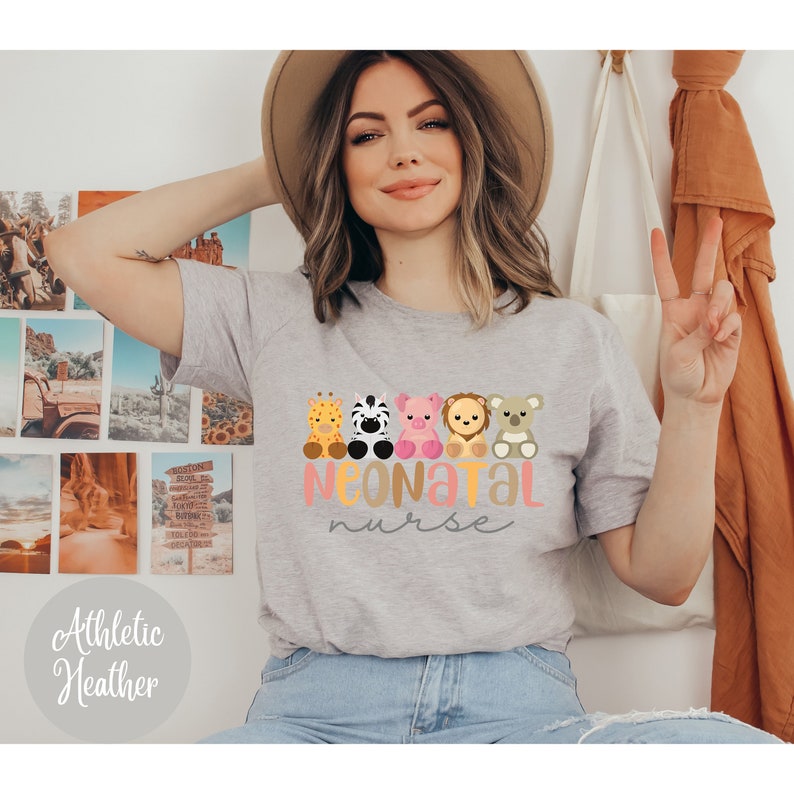Puede incluir: Una camiseta gris con un gr&aacute;fico de cinco animales de dibujos animados y el texto "NEONATAL nurse". Los animales son una jirafa, una cebra, un cerdo, un le&oacute;n y un koala. La camiseta es de color gris jaspeado.