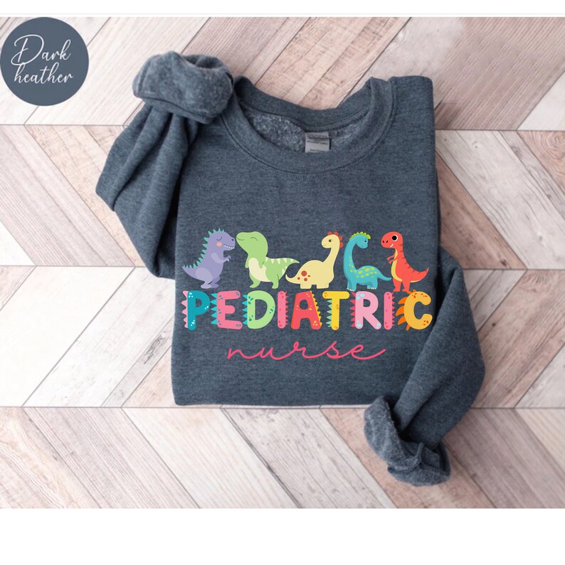 May include: Dark heather grey sweatshirt with a colorful graphic of dinosaurs and the text "PEDIATRIC nurse".
