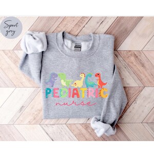 May include: A gray sweatshirt with a graphic of colorful dinosaurs and the text "PEDIATRIC nurse" in pink.
