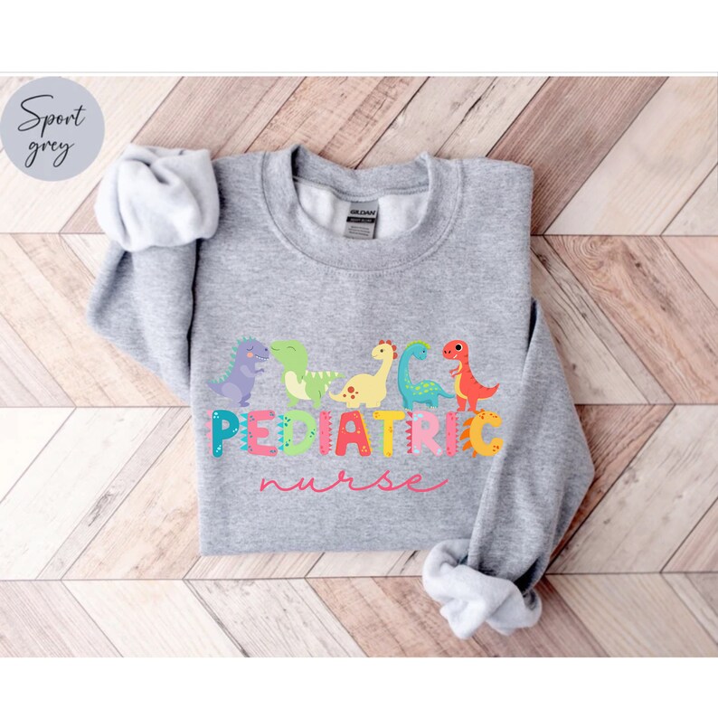 May include: A gray sweatshirt with a graphic of colorful dinosaurs and the text "PEDIATRIC nurse" in pink.