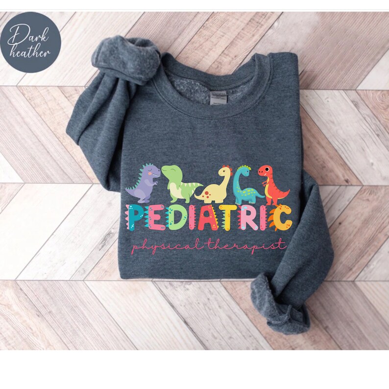May include: A dark heather gray sweatshirt with a graphic print of colorful dinosaurs and the text 'PEDIATRIC physical therapist'.