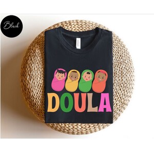 May include: Black t-shirt with a graphic of four babies in colorful swaddles and the word "DOULA" in colorful letters.