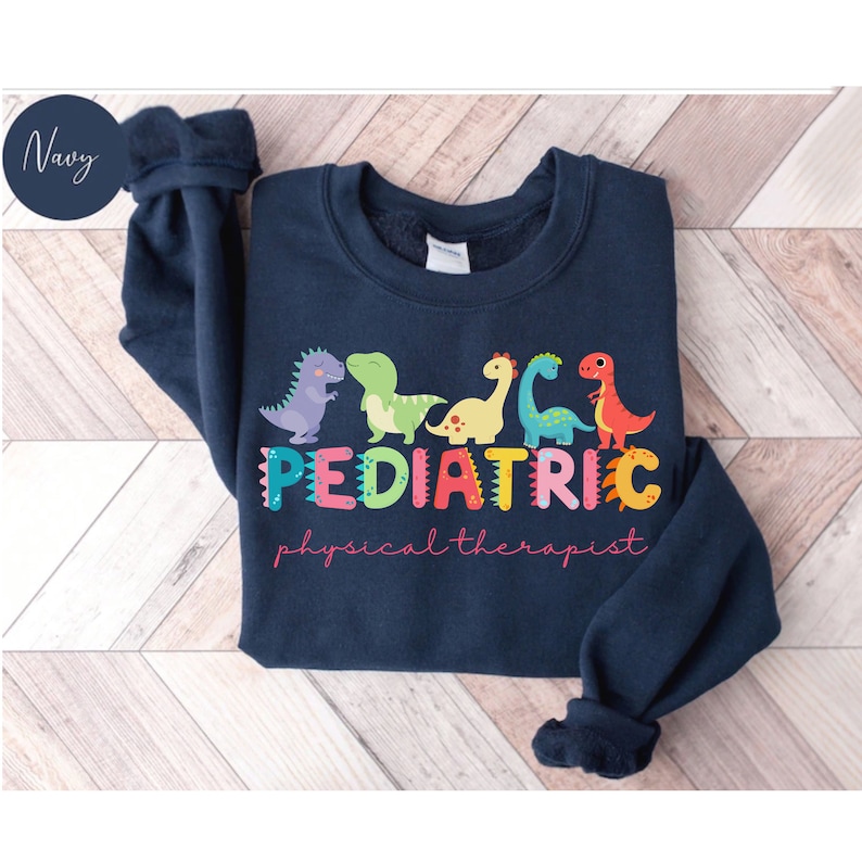 May include: A navy blue sweatshirt with a colorful dinosaur design and the text 'PEDIATRIC physical therapist'.
