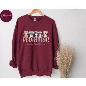 Puede incluir: Una sudadera color granate con un gr&aacute;fico de cinco animales de dibujos animados y el texto "pediatric nurse".