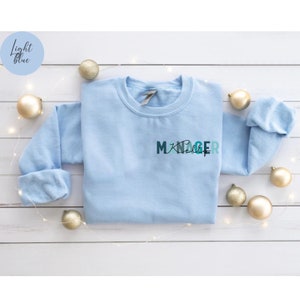 May include: Light blue sweatshirt with the text "MANAGER" in a gradient of blue and green colors.