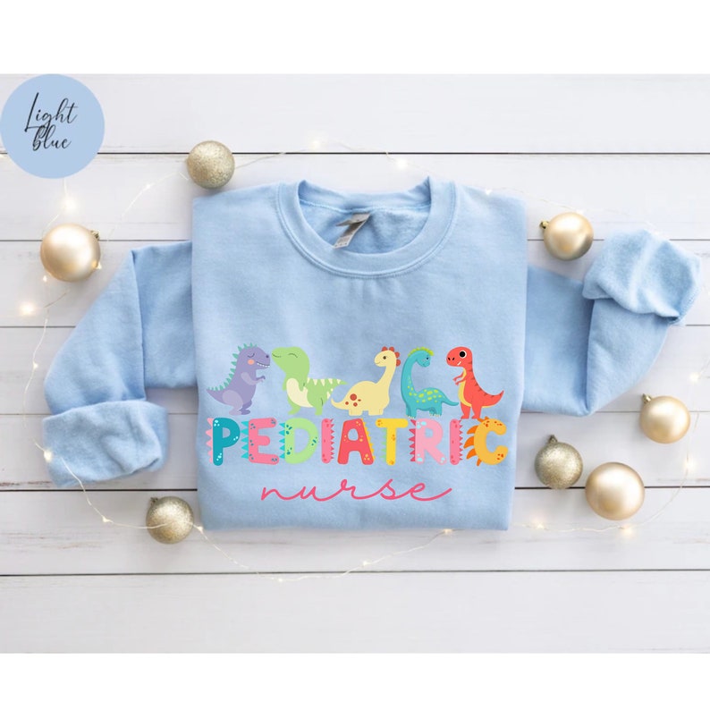 May include: Light blue sweatshirt with a graphic of colorful dinosaurs and the text "PEDIATRIC nurse".