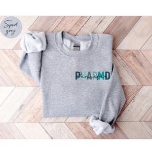 May include: A gray sweatshirt with the word "PHARM.D" in colorful letters and the name "Jennifer" written underneath.