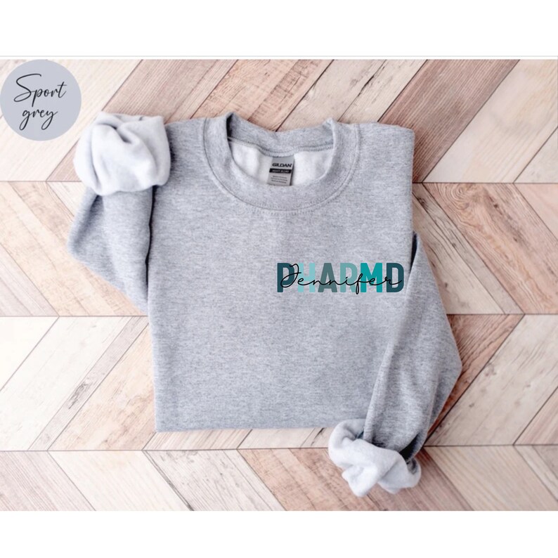 May include: A gray sweatshirt with the word "PHARM.D" in colorful letters and the name "Jennifer" written underneath.