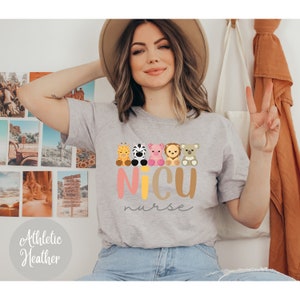 May include: A gray t-shirt with a graphic of five cartoon animals sitting in a row. The animals are a giraffe, zebra, pig, lion, and koala. The text "NICU nurse" is written below the animals in pink and yellow letters.