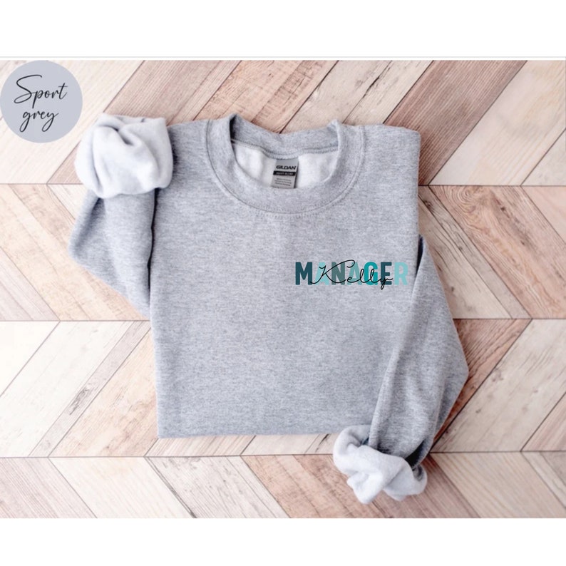 May include: A gray sweatshirt with the word "MANAGER" printed on the front in a blue and green gradient.