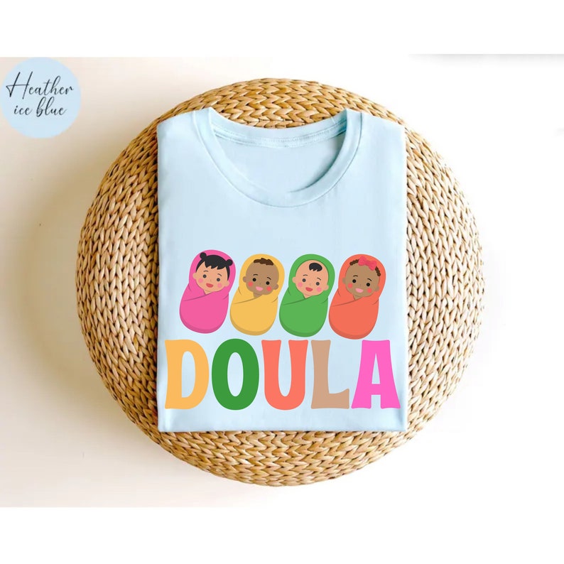 May include: Light blue t-shirt with a graphic of four babies in colorful swaddles and the word "DOULA" in colorful letters.