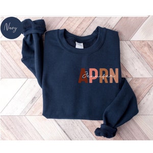 May include: A navy blue sweatshirt with the text 'Jennifer APRN' in brown, pink, and orange letters.