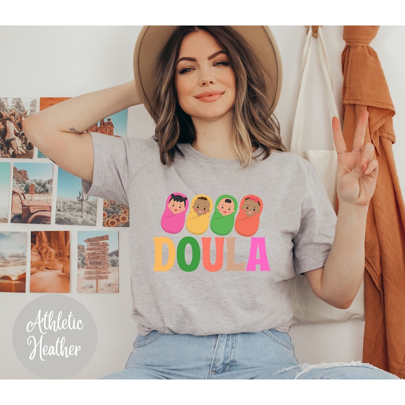 May include: A gray t-shirt with a graphic of four babies in swaddles and the word "DOULA" in colorful letters.