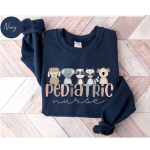 Puede incluir: Sudadera azul marino con una l&iacute;nea de animales de dibujos animados y el texto "Pediatric Nurse".
