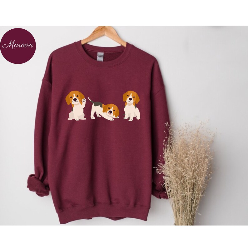 May include: A maroon sweatshirt with a graphic of three beagle puppies. The puppies are in different poses, one is sitting, one is standing, and one is lying down.