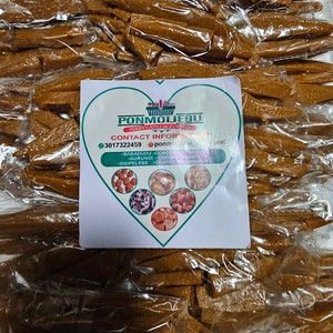 May include: A tray of individually wrapped, golden-brown candy pieces. The candy is in clear plastic packaging. A white card with green accents and text is placed on top of the candy, listing the brand and contact information.