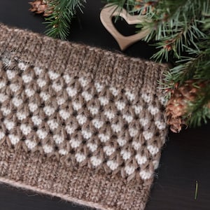 Pode incluir: Um chapéu de malha marrom e branco com um padrão texturizado. O chapéu é feito com um fio macio e tem uma sensação quente e aconchegante.