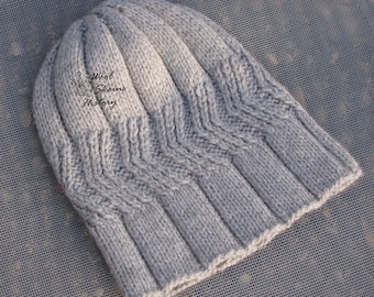 May include: A light gray knitted beanie hat with a ribbed brim and a textured chevron pattern. The hat has the text "Wool Skeins History" on the side. The hat is made of soft yarn.