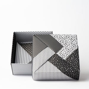 May include: A black and white origami box with a geometric pattern. The box is open and the lid is folded back.