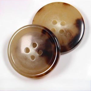 May include: Two large, round buttons with a tortoiseshell pattern. The buttons are a mix of light and dark brown, with four holes for sewing. The buttons have a glossy finish and are slightly overlapping.