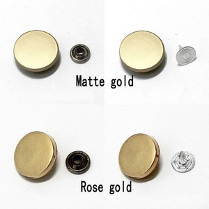 May include: Two sets of gold-toned metal snap buttons, one set in matte gold and one set in rose gold. Each set includes a button, a post, and a cap.