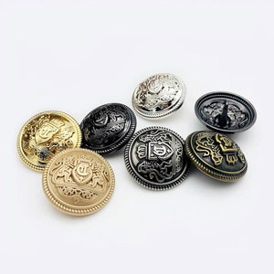 Puede incluir: Surtido de seis botones metálicos decorativos con un diseño en relieve que presenta una corona y un escudo con una letra "S" en su interior. Los botones están en varios acabados, incluyendo oro, plata y negro.