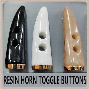 May include: Three resin horn toggle buttons in black, white, and tan. Each button has two holes and a gold-colored base. The text "RESIN HORN TOGGLE BUTTONS" is at the bottom of the image.