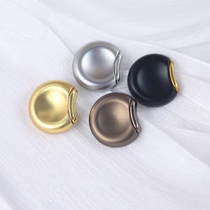 May include: Four round, metal, pocket-sized lighters in silver, black, gold, and brown.