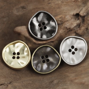May include: Four metal buttons with a textured, wavy surface. The buttons are in different colors: gold, silver, black, and dark gray.