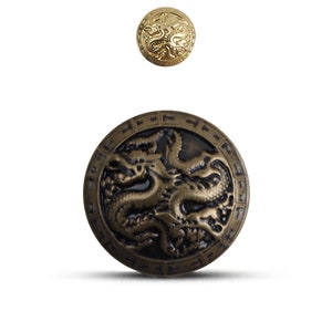 K&ouml;nnte beinhalten: Zwei runde Metallkn&ouml;pfe mit einem Drachenmotiv. Der gr&ouml;&szlig;ere Knopf ist bronzefarben mit einem schwarzen Drachen und einem schwarzen Rand. Der kleinere Knopf ist golden mit einem goldenen Drachen.