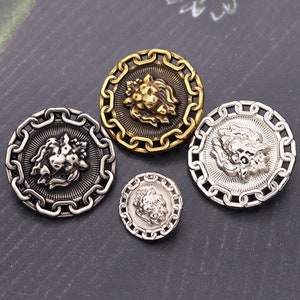 Puede incluir: Cuatro botones decorativos con un diseño de cabeza de león. Los botones están hechos de metal y tienen un borde de cadena. Los botones son de diferentes tamaños y colores, incluyendo oro y plata.