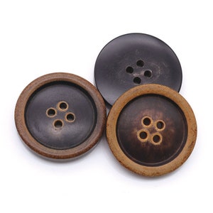 Puede incluir: Tres botones redondos de madera con cuatro agujeros cada uno. Los botones son marrones con un centro marrón más oscuro y un anillo exterior marrón claro.