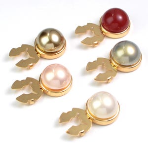 Puede incluir: Cinco gemelos decorativos para camisa con cierres de metal dorado. Los gemelos tienen un diseño abovedado en varios colores: perla, rosa, dorado, rojo y gris. Los gemelos están sobre un fondo blanco.