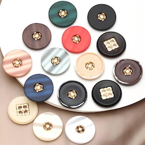 May include: A collection of various round buttons in shades of red, green, black, brown, and cream. Each button has a gold-colored center. Some buttons are square with a gold design. The buttons are arranged on a white surface.