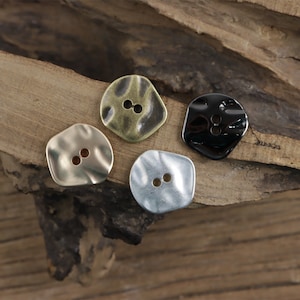 May include: Four metal buttons with a textured, wavy surface. The buttons are in gold, silver, black, and a light gold color. Each button has two holes.