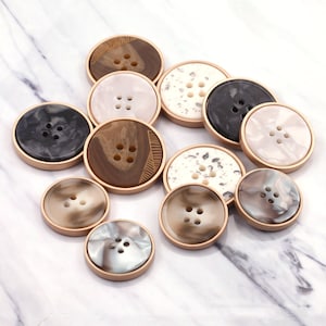 Può includere: Assortimento di 12 bottoni decorativi in ​​vari colori e motivi, tra cui marrone, nero, bianco e beige. I bottoni hanno un bordo dorato e quattro fori.