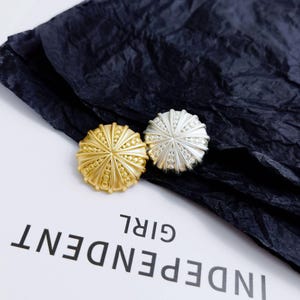 May include: Two decorative buttons, one gold and one silver, with a sunburst design. The buttons are on a black background with the text "INDEPENDENT GIRL" visible.