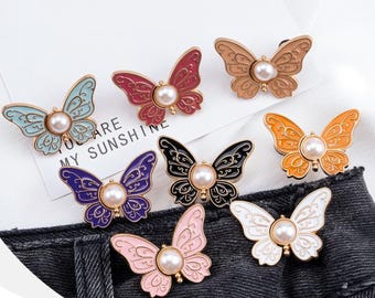 May include: A collection of butterfly-shaped brooches in various colors, including blue, red, brown, orange, black, purple, pink, and white. Each brooch features a pearl in the center and intricate wing detailing. The text "YOU ARE MY SUNSHINE" is visible.