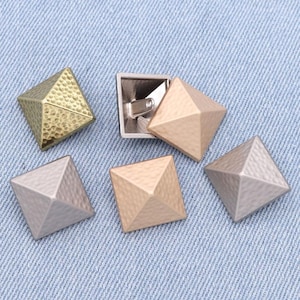 May include: Five pyramid-shaped metal embellishments in various colors, including gold, silver, and copper. The embellishments have a textured surface and are ideal for adding a decorative touch to clothing, bags, or other crafts.