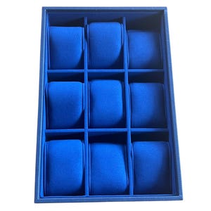 Peut inclure: Un coffret bleu pour montres avec neuf compartiments. Chaque compartiment contient un coussin bleu rembourré pour maintenir une montre. Le coffret est rectangulaire et possède un extérieur texturé.
