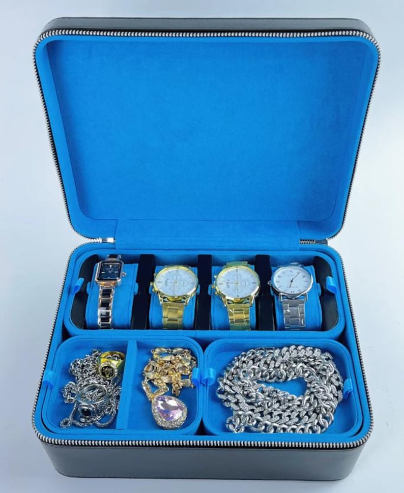 May include: Black leather watch box with blue velvet lining. The box has five slots for watches and three compartments for jewelry. The compartments contain a silver chain, a gold chain, and a pink crystal pendant.