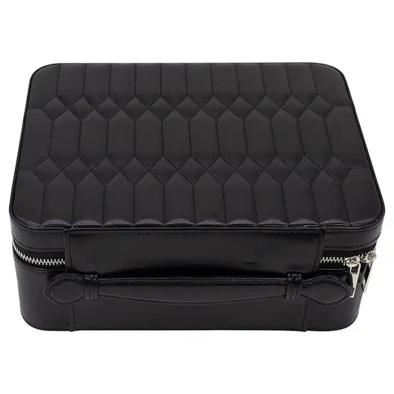May include: A black quilted leather travel case with a silver zipper and a handle. The case has a diamond-shaped pattern.
