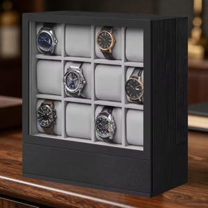 May include: A black wooden watch display case with a glass front, featuring twelve individual compartments with light gray cushions. Six wristwatches with various metallic and leather bands are arranged inside the storage organizer box.