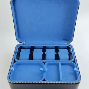 May include: Black leather watch box with a zipper closure. The interior is lined with blue velvet and has six slots for watches and two compartments for other accessories.