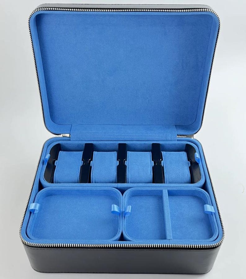 May include: Black leather watch box with a zipper closure. The interior is lined with blue velvet and has six slots for watches and two compartments for other accessories.