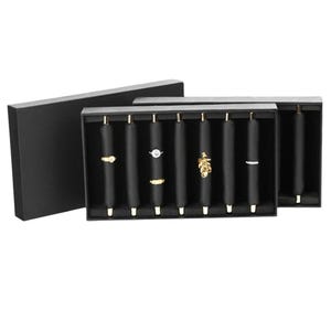 May include: A black jewelry display box with a lid, showcasing several black ring holders. Each holder displays a different ring, including gold and silver designs. The box is open, revealing the rings, and the background is white.