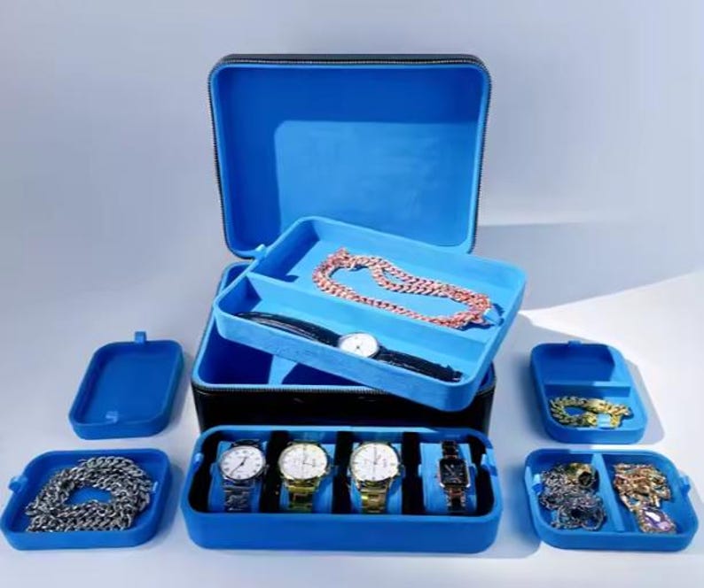 May include: A blue and black jewelry box with multiple compartments for storing watches, necklaces, and other jewelry. The box has a velvet lining and a zipper closure.