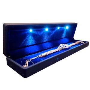 May include: A blue velvet lined jewelry box with a silver bracelet inside. The box has three blue LED lights that illuminate the interior.