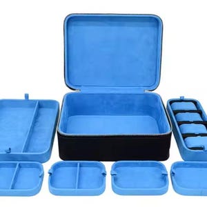 May include: A blue velvet lined watch box with a zipper closure. The box has multiple compartments for storing watches and other jewelry. The box is made of black hard plastic.